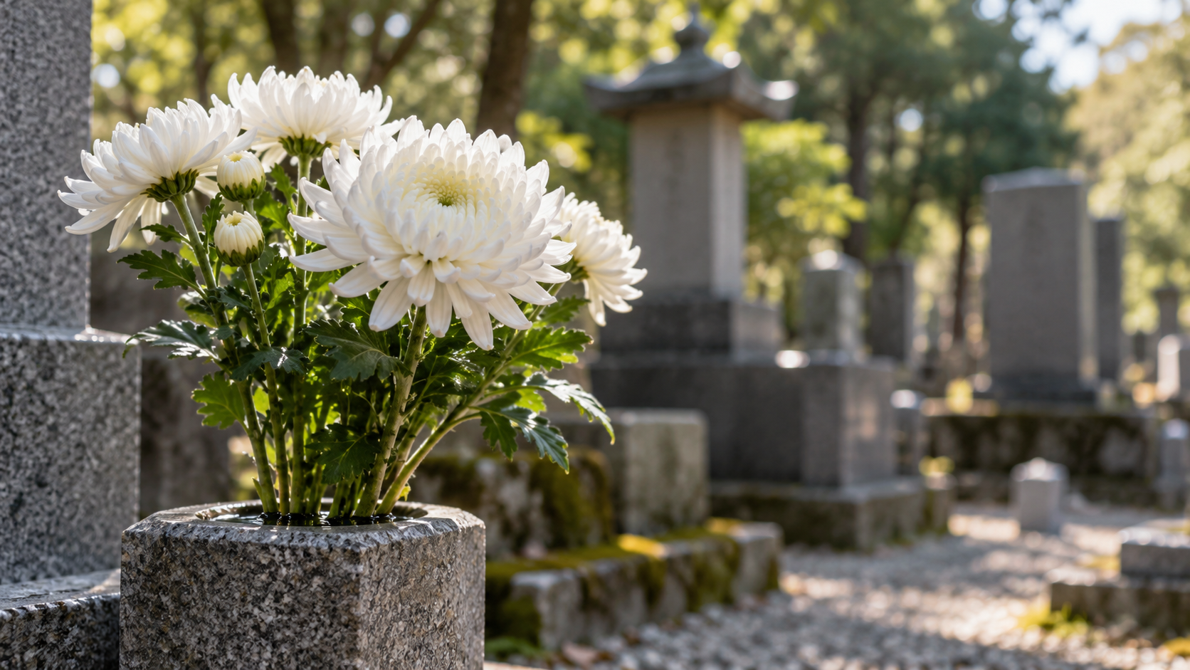 石の花器に供えられた白い菊と、背景にぼけて見える墓地の創作景観